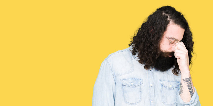 Young hipster man with long hair and beard wearing glasses tired rubbing nose and eyes feeling fatigue and headache. Stress and frustration concept.