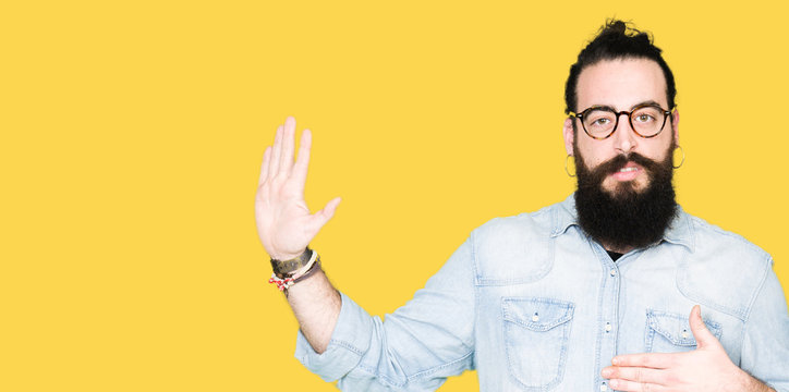 Young hipster man with long hair and beard wearing glasses Swearing with hand on chest and open palm, making a loyalty promise oath