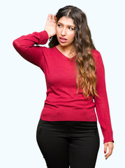 Young beautiful woman wearing red sweater smiling with hand over ear listening an hearing to rumor or gossip. Deafness concept.