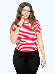 Young beautiful woman wearing glasses touching mouth with hand with painful expression because of toothache or dental illness on teeth. Dentist concept.