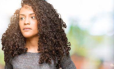 Young beautiful woman with curly hair wearing grey sweater with hand on stomach because indigestion, painful illness feeling unwell. Ache concept.