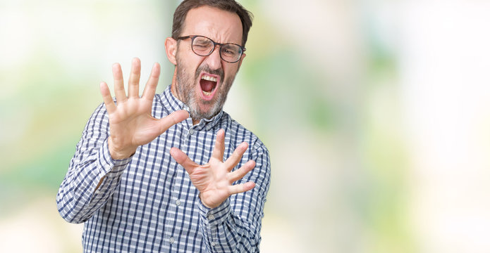 Handsome middle age elegant senior business man wearing glasses over isolated background afraid and terrified with fear expression stop gesture with hands, shouting in shock. Panic concept.