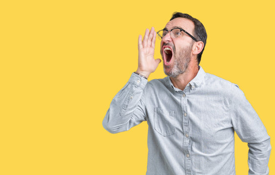 Handsome middle age elegant senior man wearing glasses over isolated background shouting and screaming loud to side with hand on mouth. Communication concept.