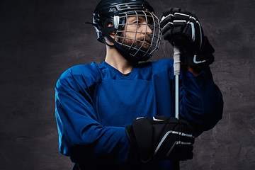 Portrait of a bearded ice-hockey player in a blue sportswear with gaming stick. Studio shot.