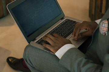 Businessman wearing suite holding laptop on his lap and looking into banking charts 