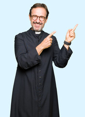 Middle age priest man wearing catholic robe smiling and looking at the camera pointing with two...