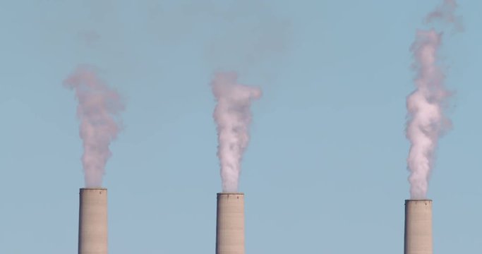 Three smokestacks in a row spewing carbon dioxide pollution into the air from a coal-burning power plant