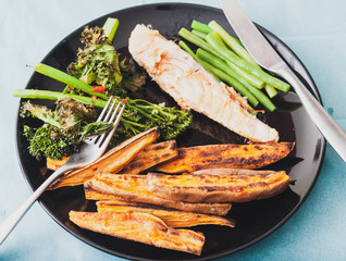 Overhead view of sweet potato wedges and salmon fillet served with tenderstem broccoli and green beans