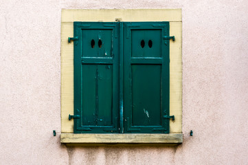 Fototapeta premium Hausfassade mit grünem geschlossenem Fensterladen aus Holz mit 4 ovalen Lichtöffnungen