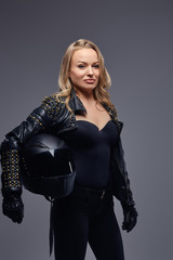 Fototapeta na wymiar Fashion, sport, extreme. Confident woman wearing racer costume holding a protective helmet, posing in a studio on a gray background.