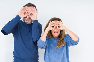 Beautiful middle age couple in love over isolated background doing ok gesture like binoculars sticking tongue out, eyes looking through fingers. Crazy expression.