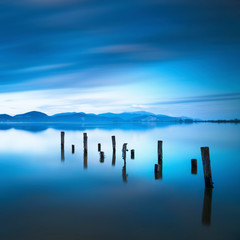 Obrazy na Szkle  Drewniane molo lub molo pozostaje na niebieskim jeziorze zachód słońca i niebo odbicie na wodzie. Versilia Toskania, Włochy