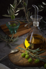 Extra virgin olive oil in glass bottle with branch of olives on rustic background. low key