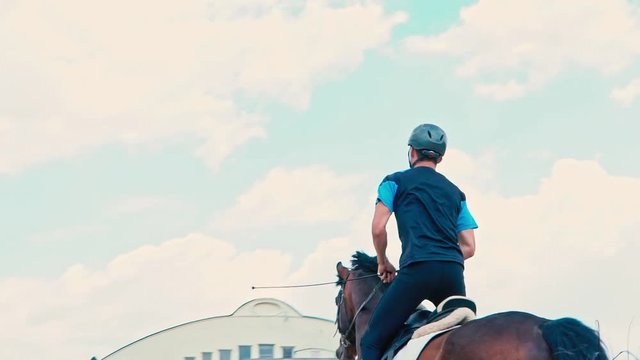 A young man on a horse jumps over obstacles. Slow motion. Training horses before the competition.  Horse Racing. Horse breeding. Farm. Horseman. Rider, equestrian, jockey