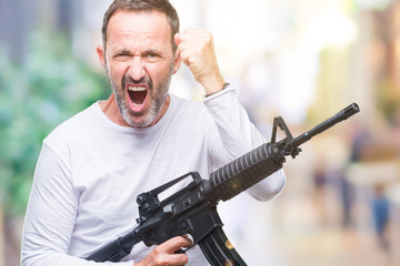 Middle age senior hoary criminal man holding gun weapon over isolated background annoyed and frustrated shouting with anger, crazy and yelling with raised hand, anger concept