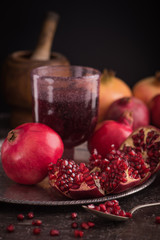 A glass of pomegranate juice with fresh pomegranate fruits and seeds on rustic background. low key