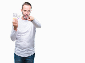 Senior hoary man holding buch of dollars over isolated background pointing with finger to the camera and to you, hand sign, positive and confident gesture from the front
