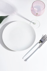 White plate and cutlery on a light table. Cretive minimalistic concept.