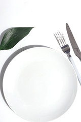 White plate and cutlery on a light table. Cretive minimalistic concept.