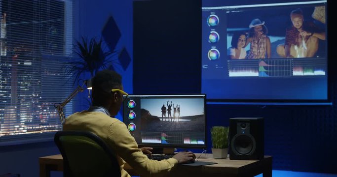 Medium shot of a young man editing video inside the modern video studio while his colleagues are giving instructions