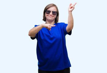 Young adult woman with down syndrome wearing sunglasses over isolated background smiling and looking at the camera pointing with two hands and fingers to the side.