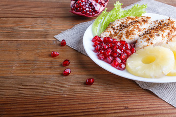 Fried chicken fillets with lettuce, pineapple and pomegranate seeds on brown wooden background.
