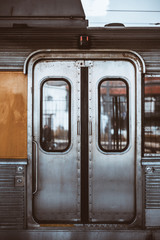 Vertical shot of the metal grungy closed automatic doors of a chrome carriage trim of a European suburban train with windows, two buttons for opening, handhold, and a round lock below