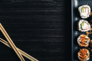 Sushi rolls with chopsticks and soy sauce on dark background. Space text