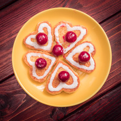 A flower laid out of heart-shaped cookies with frozen cherries on top