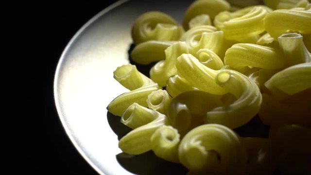 Raw macaroni in rotation. Elbow macaroni. Macaroni rigati close up.  Raw pasta  black background. Italian cuisine concept.