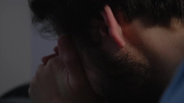 A man with a beard kneeling by his bed with hands on his face, whilst praying and crying. ZOOM IN, CLOSEUP SHOT.