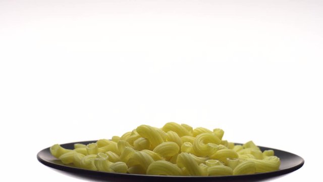 Raw macaroni in rotation. Elbow macaroni.  Macaroni rigati close up.  Raw pasta  isolated on white. Italian cuisine concept.