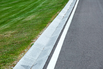 Street gutter of a stormwater drainage system on the side of an road with markings and grass.