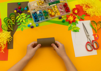 Child makes craft tree of paper. Orange background and materials for creative classes.