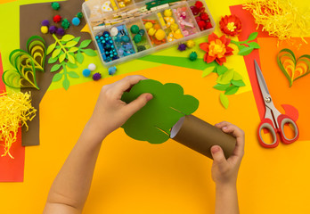 Child makes craft tree of paper. Orange background and materials for creative classes.