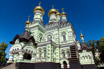 Fototapeta na wymiar Orthodox church building with a green facade and golden domes against a blue sky, the architecture of the bottom-up view.