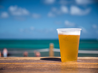 Beer in plastic cup on wooden table over caribbean sea background