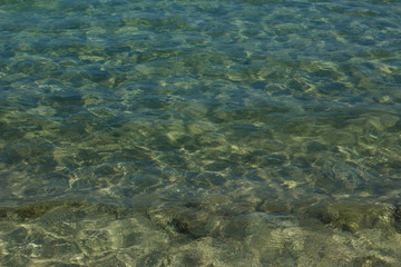 shallow stone lake water coast line bottom background with small glares sun reflection on surface