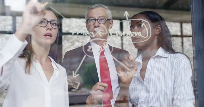 4K Multiracial business team drawing on glass, exploring business solutions. Slow motion.