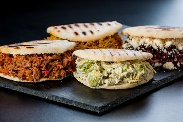Venezuelan Latin American food, 4 arepas of different stuffing on a black table. Arepa with mechada meat, queen pepeada, black beans with white cheese and chicken
