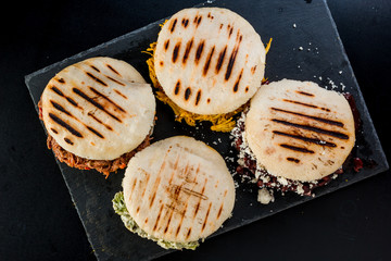 Venezuelan Latin American food, 4 arepas of different stuffing on a black table. Arepa with mechada meat, queen pepeada, black beans with white cheese and chicken