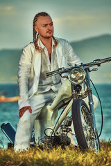 Young man with vintage custom motorbike on the tropical coast background