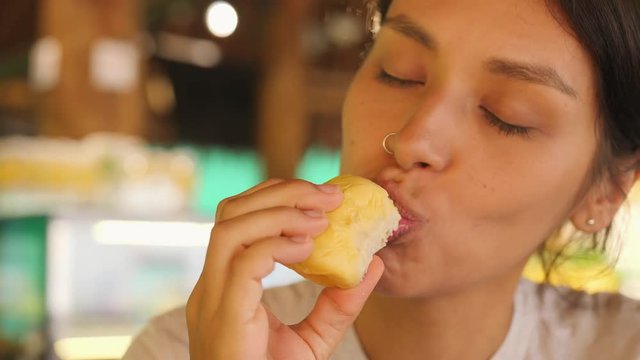 Young Tourist Woman Trying Durian First Time. Female Holding Piece of Durian Pulp and Sniffing It Enjoying Good Sweet Smell. 4K. Kuala Lumpur, Malaysia.