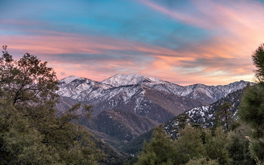 Snowy California mountain sunset with pink and purple wispy clouds and green trees