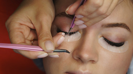 Obraz na płótnie Canvas Cosmetic procedure for eyelash extensions in spa salon. Beautician makes correction of volume and length of eyelashes. Shooting close-up.