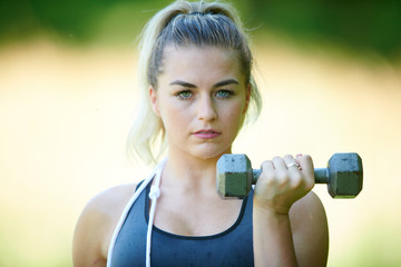 Stunning young blonde woman working out in summer heat - doing bicep curl - fitness sweat glistening on skin