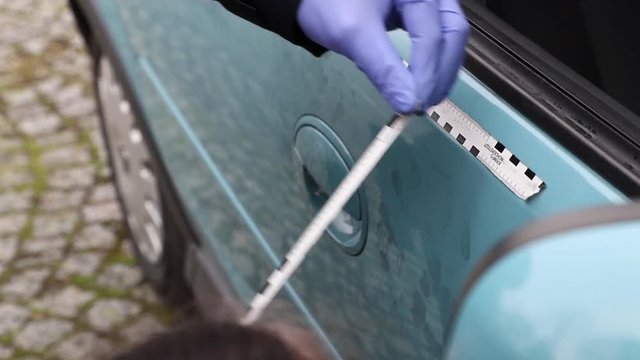 Crime Scene Unit officer collecting fingerprints and evidence on a vehicle which was damaged by criminals.