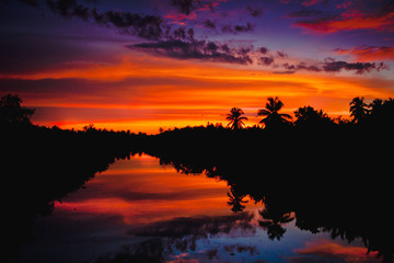 colorful sunset with clouds light rays over the river with reflections on silhouette nature landscape background 