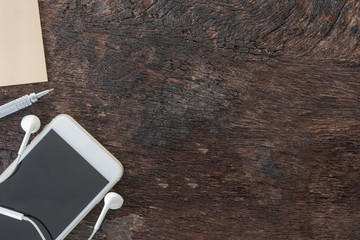 Top view laptop, smartphone, post note, pencil and earphone on old wooden background with copy space