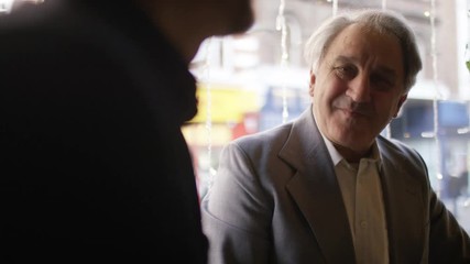Handheld shot of a group of men at a table in a coffee shop or wine bar in conversation